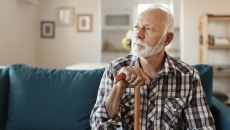   Person sitting on a couch looking away from the camera while holding a wooden cane