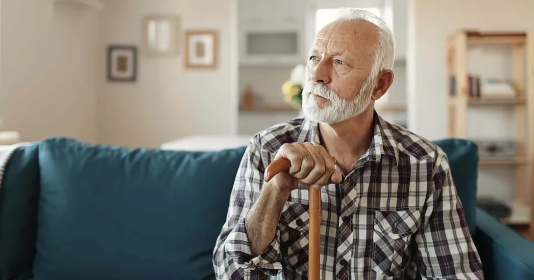   Person sitting on a couch looking away from the camera while holding a wooden cane