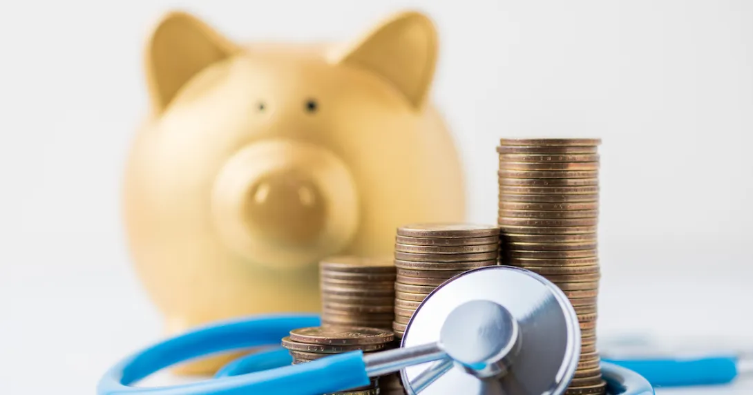   A piggy bank next to a pile of coins and a stethoscope.