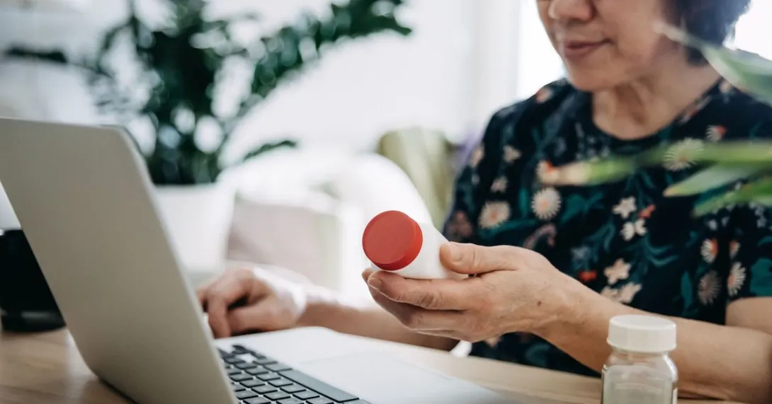   A person holding a pill bottle while using a laptop.